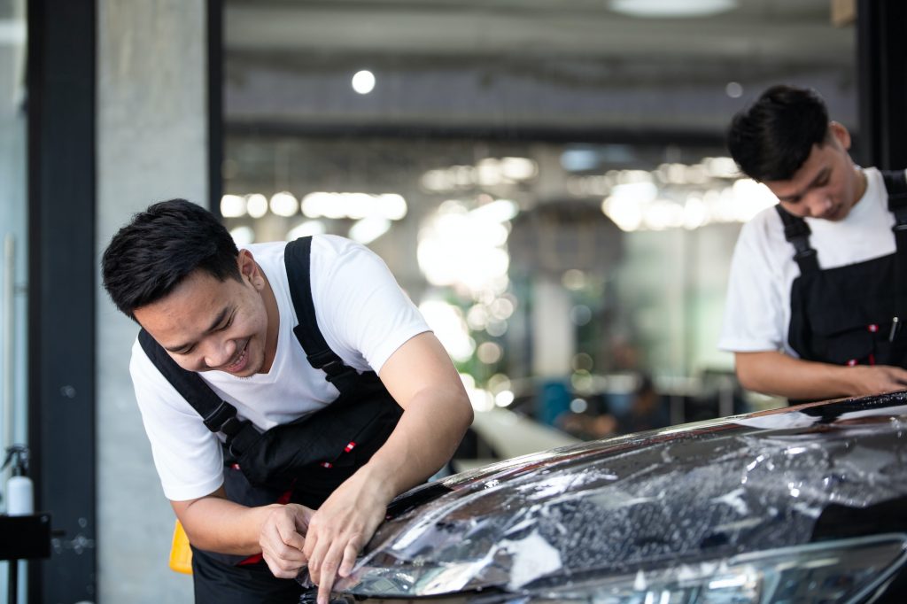 Detailing film specialist cutting and wrapping car at auto repair shop